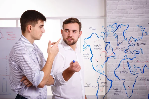 Two concetrated young businessmen talking and writing on glass board in office. The concept of business presentations.