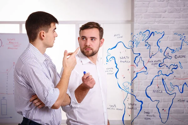 Twee geconcentreerde jonge ondernemers praten en schrijven op glas bord in office. Het concept van zakelijke presentaties. — Stockfoto