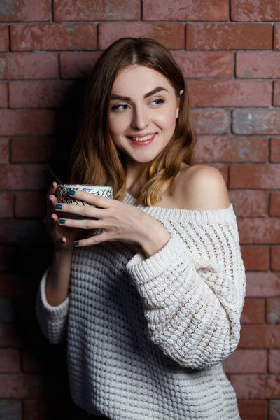 Young beautiful woman drinking a cup of coffee in the cafe on a red brick wall background. Stylish lady with hot drink.