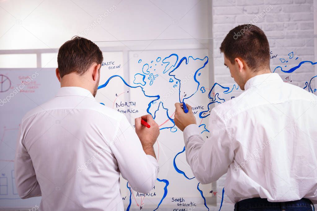 Two concetrated young businessmen talking and writing on glass board in office. The concept of business presentations.