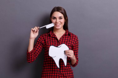 Gri bir arka plan üzerinde büyük bir diş ve diş fırçası bir kağıt kart tutan genç mutlu bir kadın. Tıp ve diş hekimi kavramı ziyaret.
