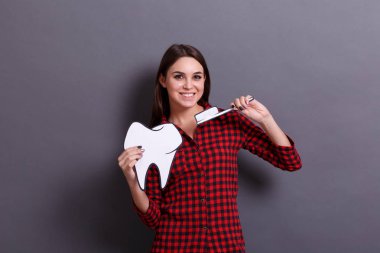 Neşeli bir kadın bir diş ve diş fırçası bir kağıt görüntüsü gri bir arka plan üzerinde tutar. Sağlık kavramı.