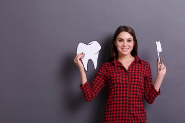 Neşeli bir kadın bir diş ve diş fırçası bir kağıt görüntüsü gri bir arka plan üzerinde tutar. Sağlık kavramı.