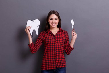 Neşeli bir kadın bir diş ve diş fırçası bir kağıt görüntüsü gri bir arka plan üzerinde tutar. Sağlık kavramı.
