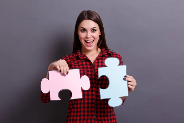 Молода дівчина показує різнокольорові шматочки головоломки, на сірому фоні. Концепція успішного вирішення проблем . — стокове фото
