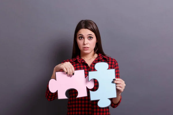 Una joven que muestra piezas coloridas de un rompecabezas, sobre un fondo gris. Solución de problemas de éxito concepto . — Foto de Stock