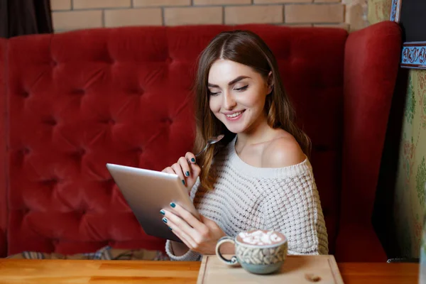 Kafede kırmızı kanepede bir tablet ile neşeli bir esmer kadın. İş ve eğitim kavramı. — Stok fotoğraf