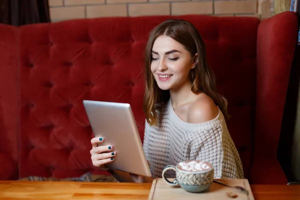 Kafede kırmızı kanepede bir tablet ile neşeli bir esmer kadın. İş ve eğitim kavramı. — Stok fotoğraf