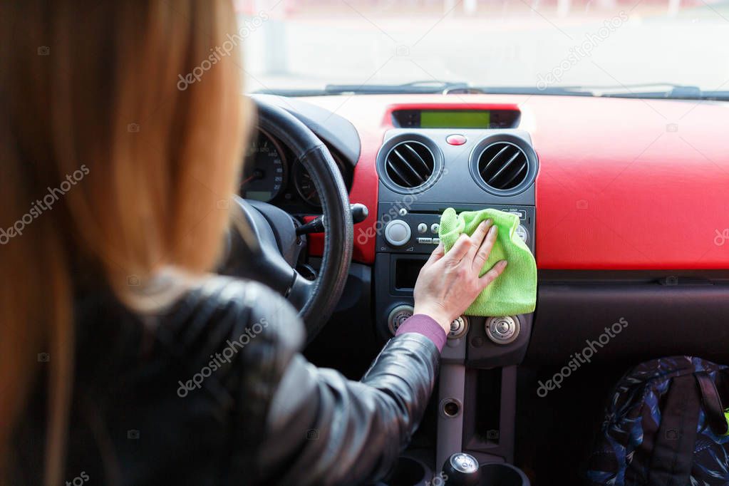 A young woman wipes the dust with a green rag in the car. Dry cleaning of the car panel, car washing.Woman cleaning car dashboard.