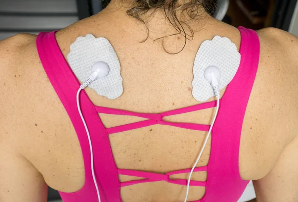 Woman using a Home Electrical Nerve Stimulation Unit also Known as TENS Unit on her Upper Back