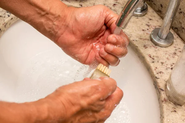 Man Washing his Hands with a Scrub Brush and Soap and Water in the Sink
