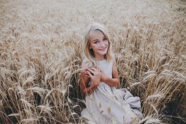 Bir buğday alanında oturan gülümseyen kız.