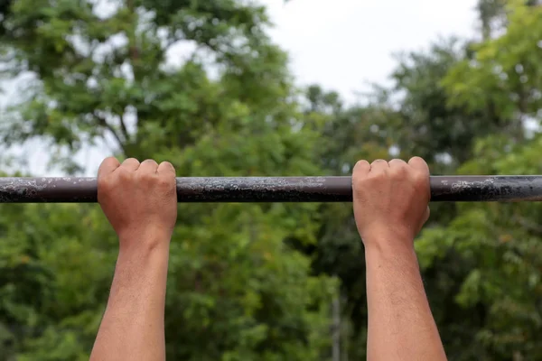 Doğa arka plan ile egzersiz için yatay çubuğu çekme yapan güçlü erkek kol