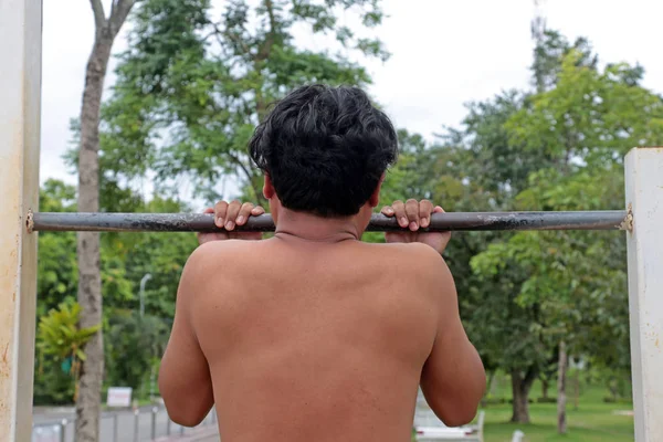 Um homem forte fazendo exercício com puxar para cima na barra horizontal em um fundo natureza — Fotografia de Stock