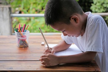 Asyalı küçük çocuk dikkatle doğa ile ahşap masa üzerinde çizim arka plan bulanıklık. Küçük ressam kavramı.