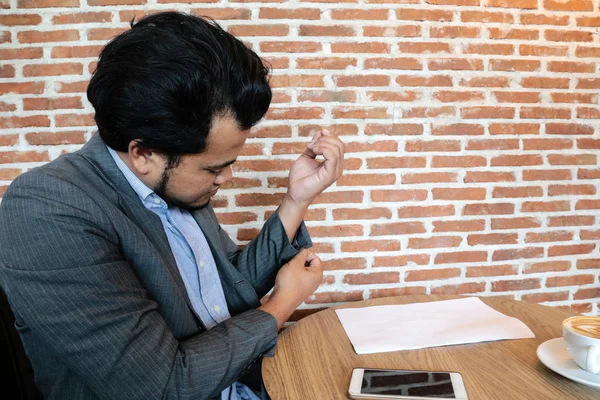 Gli uomini d'affari asiatici che mettono un pulsante alla manica di un vestito mentre si siedono davanti a un caffè di tavolo . — Foto Stock