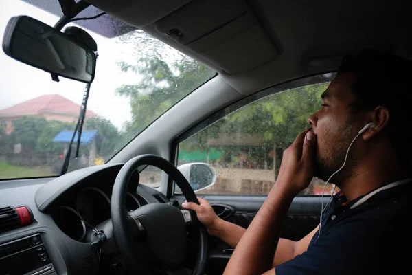 Hombre asiático con auriculares bostezando en su coche mientras conduce debido a la somnolencia . — Foto de Stock