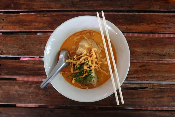 Fotoğraf ahşap masa üzerinde beyaz bir kase baharatlı erişte en iyi manzaralı. Tayland Kuzey erişte ahşap bir masaya 