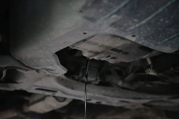 Oude en vuile motorolie wordt afgevoerd uit onder een auto tijdens een motorwissel olie. — Stockfoto