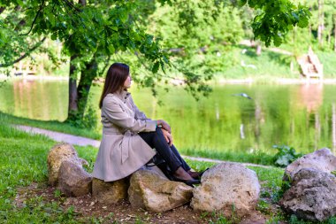 Bir kız gölün kenarında kayaların üzerinde oturuyor.