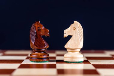 Beyaz ve siyah satranç şövalyeleri siyah arka planda satranç tahtasının üzerinde durur ve birbirlerine bakarlar.