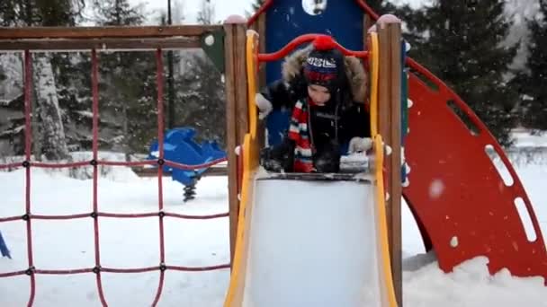Kleine jongen op de kinderspeelplaats in de winter tijd met grijze achtergrond — Stockvideo