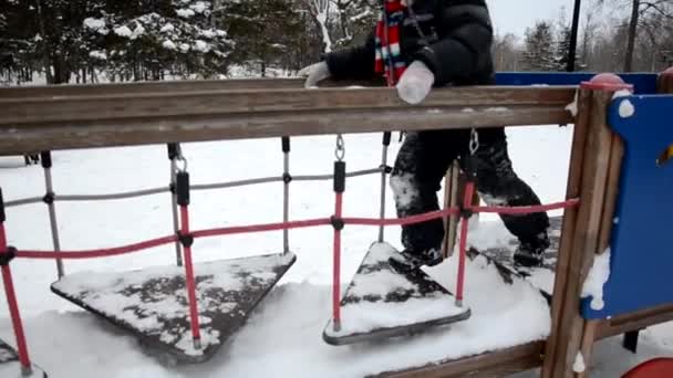 Liten pojke på barnens lekplats på vintern med grå bakgrund — Stockvideo