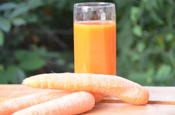 Стакан морковного сока и свежей моркови на деревянном столе на зеленом фоне — стоковое фото
