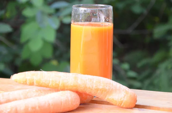 Segelas jus wortel dan wortel segar di meja kayu dengan latar belakang hijau — Stok Foto