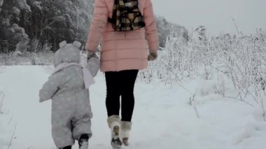 Kış Ormanı 'nda Yürüyen Aile. Küçük kız ve annesi kış ormanında yürüyorlar. Kar ve kızakla oynuyor. Sıcak kış kıyafetleri içinde
