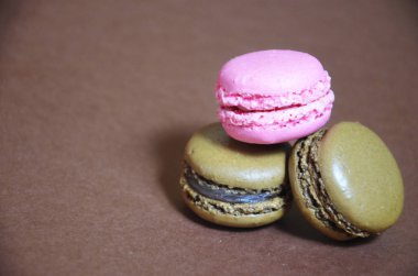 Renkli, lezzetli bir badem kurabiyesi. Kahverengi arka planda farklı renklerde makaronlar.