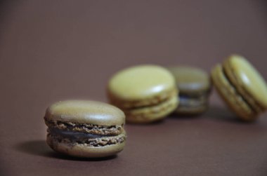 Renkli, lezzetli bir badem kurabiyesi. Kahverengi arka planda farklı renklerde makaronlar.