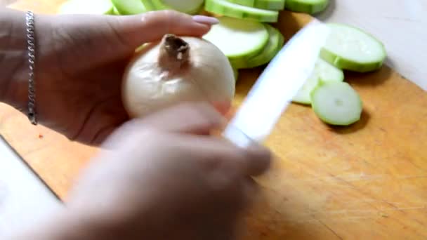 Лук крупным планом перемещается и смешивается острым блестящим ножом на коричневой рабочей поверхности на кухне — стоковое видео