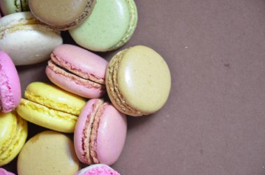 Renkli, lezzetli bir badem kurabiyesi. Kahverengi arka planda farklı renklerde makaronlar.