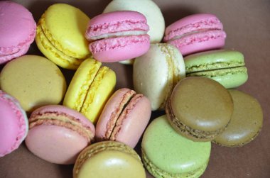 Renkli, lezzetli bir badem kurabiyesi. Kahverengi arka planda farklı renklerde makaronlar.