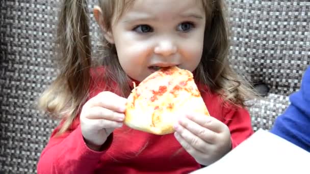 Schönes Mädchen, das Pizza isst, kleines süßes Mädchen, das in einem Café sitzt und Pizza isst. Mama sitzt neben ihr und hilft ihr beim Pizza essen. — Stockvideo