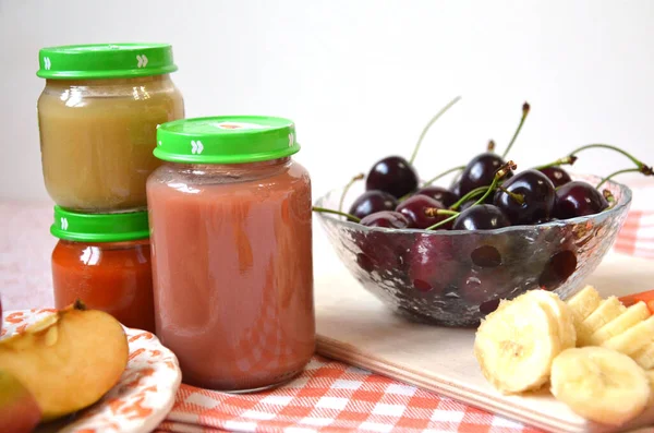 Comida para bebés, fruta del bebé triturada en un frasco de vidrio, rodajas de zanahoria, manzana, plátano, cereza — Foto de Stock