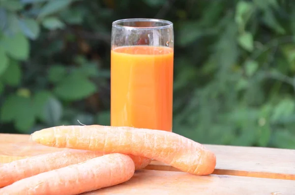 Szklanka soku marchewkowego i świeżej marchewki na drewnianym stole na zielonym tle — Zdjęcie stockowe
