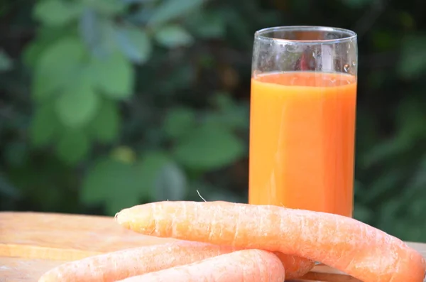 Segelas jus wortel dan wortel segar di meja kayu dengan latar belakang hijau — Stok Foto