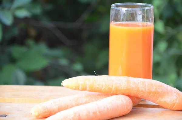 Pahar de suc de morcovi și morcovi proaspeți pe masă de lemn pe fundal verde — Fotografie, imagine de stoc