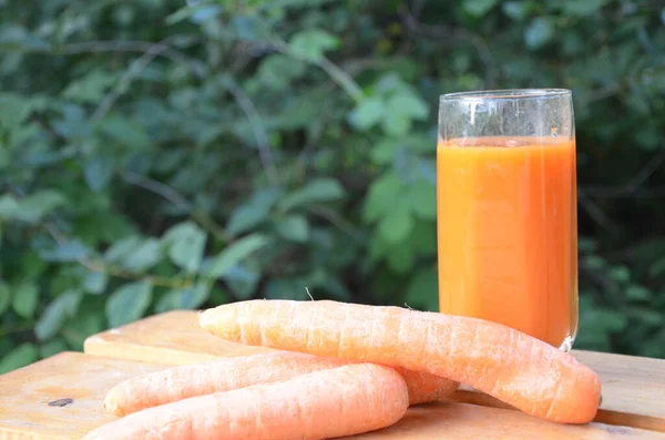 Vidro de suco de cenoura e cenouras frescas na mesa de madeira no fundo verde — Fotografia de Stock