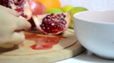 Meyve salatası için taze, sulu kırmızı bir nar kabuğu. Arka planda meyve var. Diyet, az kalori, vejetaryenlik, doğal vitaminler. Gemide eli kesilmiş bir kadının el yapımı nar resmi var. Yan görünüm.