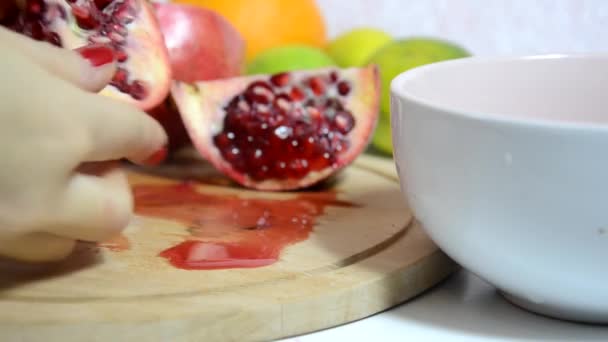 Skär och skalar färsk saftig röd granatäpple för en fruktsallad. Frukt på bakgrunden. Föda, några kalorier, vegetarianism, naturliga vitaminer. Närbild av kvinna hand skära granatäpple ombord. Sidovy. — Stockvideo