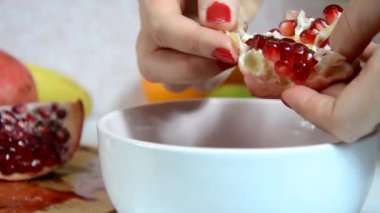 Meyve salatası için taze, sulu kırmızı bir nar kabuğu. Arka planda meyve var. Diyet, az kalori, vejetaryenlik, doğal vitaminler. Gemide eli kesilmiş bir kadının el yapımı nar resmi var. Yan görünüm.