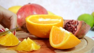 Kız bir portakalı soyar ve keser. Masada dilimlenmiş portakal, kivi ve elma var. Meyve salatası için taze kırmızı portakalı soyar ve keser. Diyet, az kalori, vejetaryenlik, doğal vitaminler..