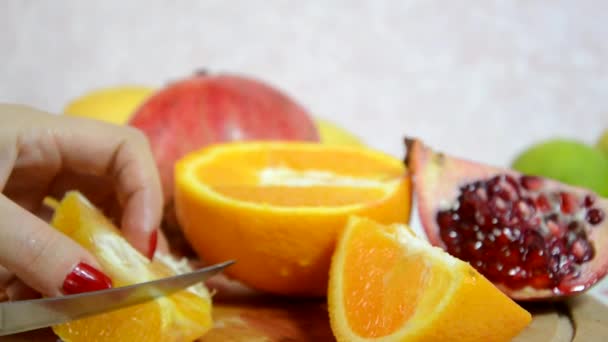 Flicka skalar och skär en apelsin. Skivad apelsin, kiwi och äpplen på bordet. skär och skalar färsk saftig röd apelsin för en fruktsallad. Föda, få kalorier, vegetarianism, naturliga vitaminer. — Stockvideo