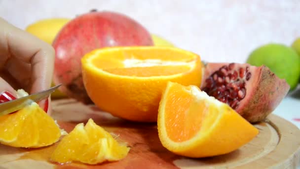 Flicka skalar och skär en apelsin. Skivad apelsin, kiwi och äpplen på bordet. skär och skalar färsk saftig röd apelsin för en fruktsallad. Föda, få kalorier, vegetarianism, naturliga vitaminer. — Stockvideo