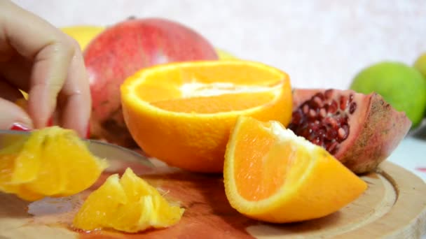 Mädchen schält und schneidet eine Orange. Auf dem Tisch Orangen, Kiwi und Äpfel in Scheiben schneiden. schneidet und schält frische saftige rote Orangen für einen Obstsalat. Ernährung, wenige Kalorien, Vegetarismus, natürliche Vitamine. — Stockvideo