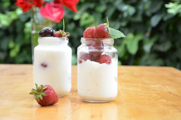 Sağlıklı kahvaltı - ev yapımı puding veya yoğurt taneciği, çilek, kiraz, hanımeli böğürtlen, fındık ve yoğurt. Vejetaryen konsept yiyecekler. Yeşil yaprakların arka planında puding ya da kokteyl.
