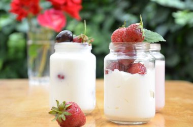 Sağlıklı kahvaltı - ev yapımı puding veya yoğurt taneciği, çilek, kiraz, hanımeli böğürtlen, fındık ve yoğurt. Vejetaryen konsept yiyecekler. Yeşil yaprakların arka planında puding ya da kokteyl.